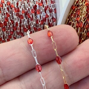 Könnte beinhalten: Nahaufnahme von zwei Schmuckketten. Eine ist silberfarben mit roten, oval geformten Perlen, die andere ist goldfarben mit ähnlichen roten Perlen. Die Ketten sind mit kleinen, rechteckigen Gliedern verbunden. Eine Rolle ähnlicher Kette befindet sich im Hintergrund.