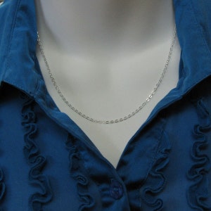 May include: A silver chain necklace on a blue shirt with ruffles.