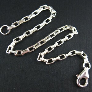 May include: A silver chain necklace with a lobster clasp and a jump ring. The chain is made of square links.
