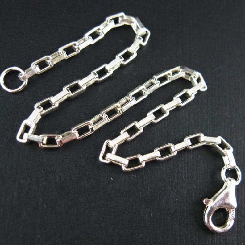 May include: A silver chain necklace with a lobster clasp and a jump ring. The chain is made of square links.