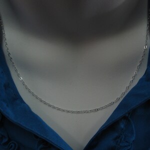 May include: A silver chain necklace on a white mannequin bust. The chain is a delicate, oval-link style.