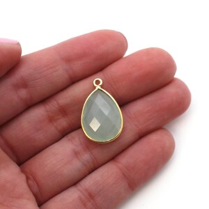 May include: A teardrop-shaped pendant with a light green gemstone set in a gold-toned metal frame.