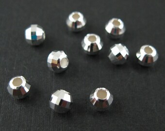 Può includere: Dieci perline rotonde sfaccettate color argento con un foro al centro. Le perline sono sparse su una superficie nera.