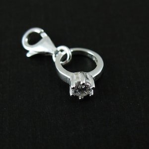 May include: Silver charm in the shape of a ring with a clear stone. The charm has a lobster clasp.
