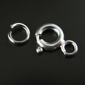 Puede incluir: Dos cierres de metal plateados para la elaboración de joyas. Uno es un simple anillo redondo, el otro es un anillo redondo con un cierre de resorte y un pequeño bucle.