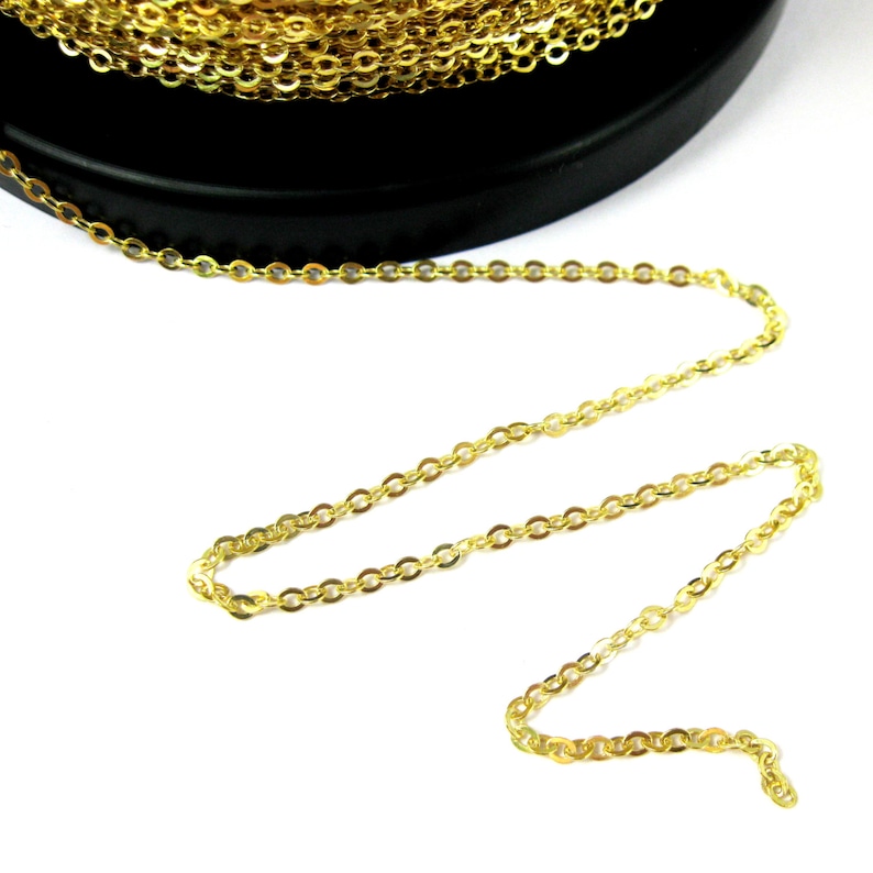 May include: A gold chain with small, oval-shaped links. The chain is coiled on a black surface and is laid out straight on a white surface.