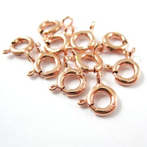 Puede incluir: Primer plano de diez cierres de langosta de oro rosa. Los cierres son pequeños y redondos, con un mecanismo de resorte. Son perfectos para sujetar joyas a cadenas o cordones.