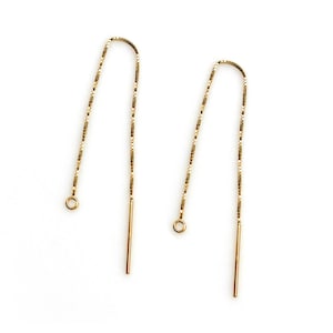 May include: A pair of gold chain earrings with a simple design. The earrings are long and thin, with a small loop at the top and a straight wire at the bottom.
