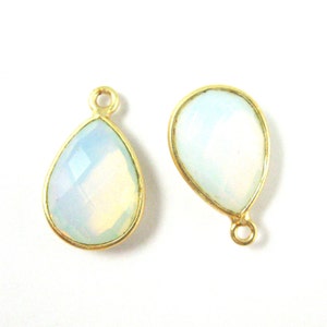 May include: Two gold-toned teardrop-shaped pendants with a white opal stone in the center. The pendants have a small loop at the top for attaching to a chain or cord.