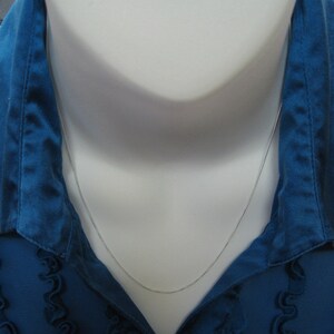 May include: A silver chain necklace on a white mannequin wearing a blue shirt.