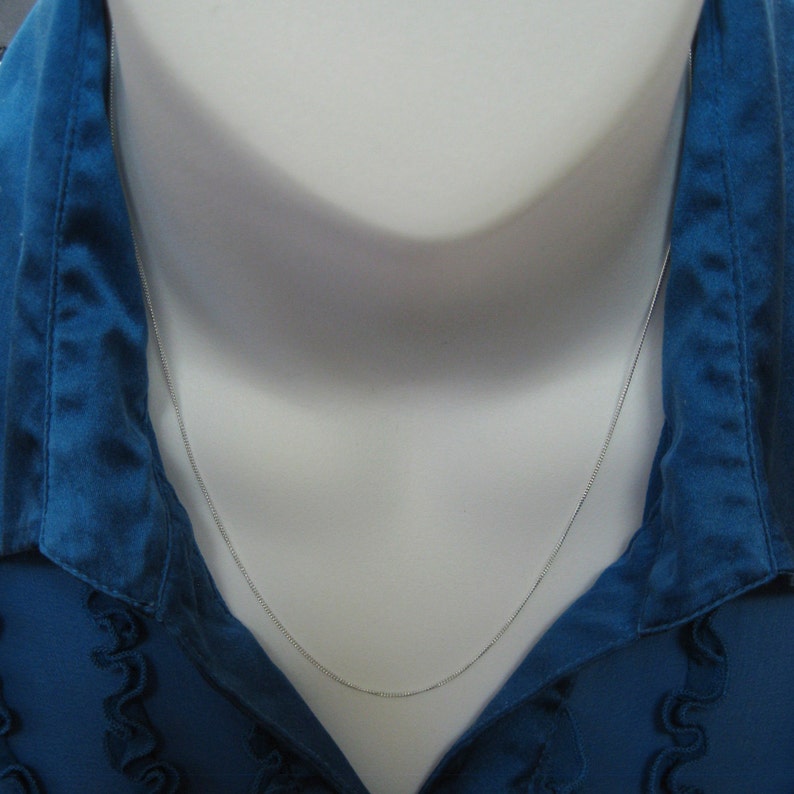 May include: A silver chain necklace on a white mannequin wearing a blue shirt.