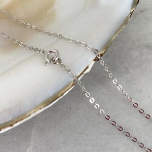 May include: A delicate silver necklace with a small clasp. The chain is made of small, interconnected oval links. The necklace is displayed on a white surface.