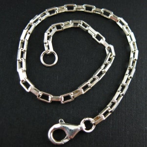 May include: A silver chain bracelet with a lobster clasp and a jump ring. The chain is made of square links.