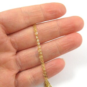May include: A gold chain necklace with a delicate, fine link design. The chain is shown draped over a hand, showcasing its length and the intricate detail of the links.