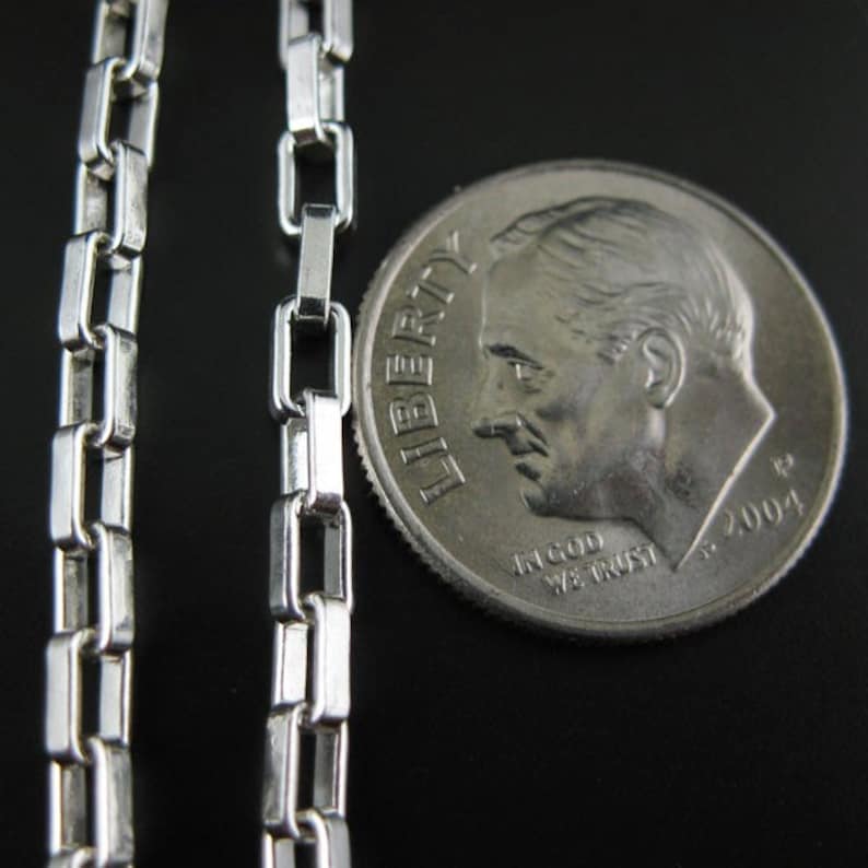 May include: A silver chain necklace with a box link design. The chain is next to a US dime coin for size comparison.