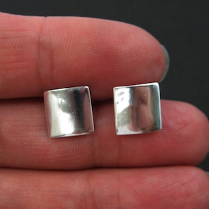 May include: A pair of silver square stud earrings. The earrings are smooth and have a shiny finish.