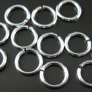 May include: A close-up of silver jump rings, a type of jewelry finding used for connecting chains, cords, and other jewelry components.