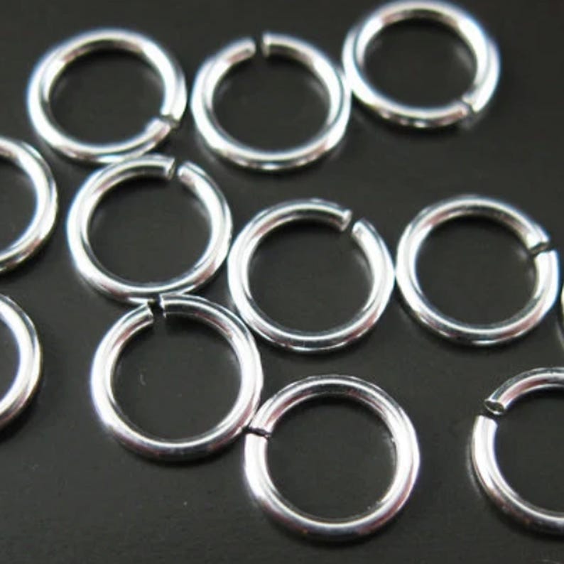 May include: A close-up of silver jump rings, a type of jewelry finding used for connecting chains, cords, and other jewelry components.