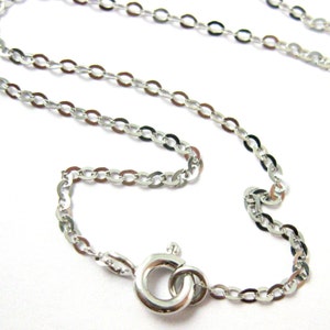 May include: A delicate silver-colored chain necklace with an oval link design. The necklace features a spring ring clasp for secure closure. The chain is displayed against a white background, highlighting its reflective surface.