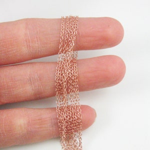 May include: A close-up of a rose gold chain, shown in a hand, with multiple strands of the chain.