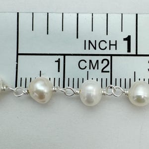 Puede incluir: Primer plano de un collar de perlas blancas de agua dulce, cada una de aproximadamente 1,3 cm de di&aacute;metro, ensartadas en un delicado alambre de plata. Las perlas se miden contra una regla marcada en pulgadas y cent&iacute;metros.