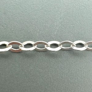 May include: Close-up of a silver-colored chain with oval links. The chain is made of a shiny, metallic material and is displayed against a gray background. The links are uniform in size and shape, creating a continuous pattern.