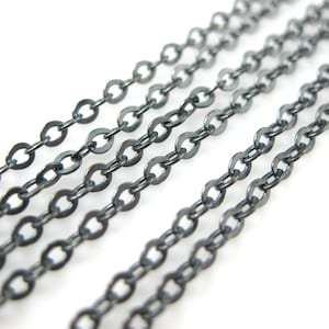 May include: Multiple strands of black oxidized chain, a type of jewelry finding, are laid out in a diagonal line on a white background.