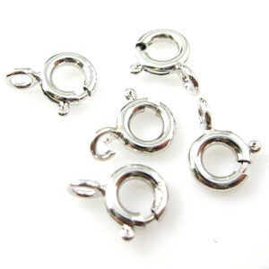 Puede incluir: Seis anillos de salto de metal plateados con un cierre de resorte. Los anillos tienen un diámetro de aproximadamente 2,5 cm.