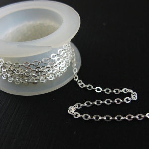 May include: A spool of silver chain, the chain is coiled around the spool and a length of chain is hanging off the spool. The chain is made of small, round links.
