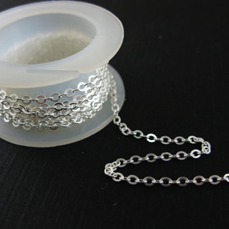 May include: A spool of silver chain, the chain is coiled around the spool and a length of chain is hanging off the spool. The chain is made of small, round links.