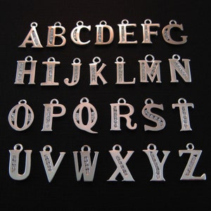 May include: Silver alphabet charms with clear rhinestones. Each charm features a letter of the alphabet, from A to Z.