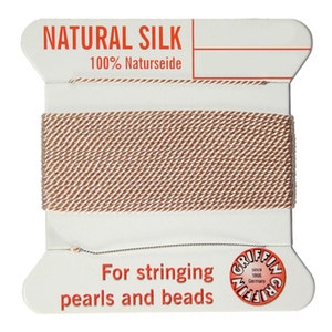 Op de afbeelding: Een spoel natuurlijke zijden draad voor het rijgen van parels en kralen. Het etiket vermeldt "NATURAL SILK 100% Naturseide" en "GRIFFIN since 1966 Germany".