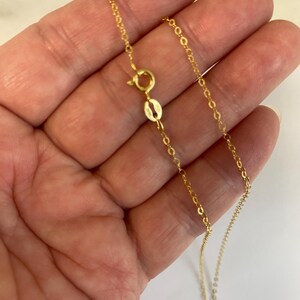 May include: A delicate gold chain necklace featuring a round spring ring clasp and a small oval tag. The chain is composed of thin, interlocking circular links that create a continuous, refined metallic strand with a polished yellow gold finish.