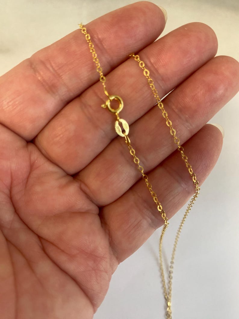 May include: A delicate gold chain necklace featuring a round spring ring clasp and a small oval tag. The chain is composed of thin, interlocking circular links that create a continuous, refined metallic strand with a polished yellow gold finish.