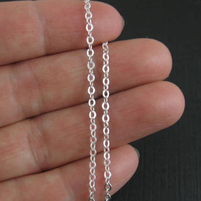 May include: A silver chain necklace with a delicate, fine link design. The chain is shown on a hand, demonstrating its size and length.