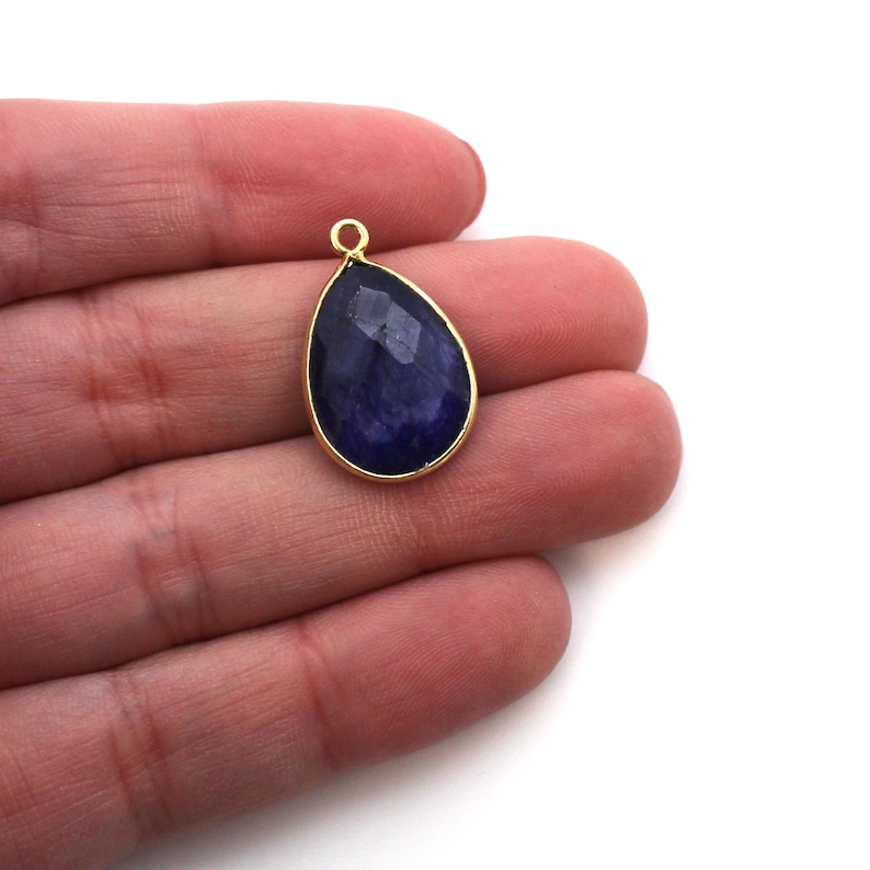 May include: A teardrop-shaped pendant with a dark blue gemstone set in a gold-toned bezel.