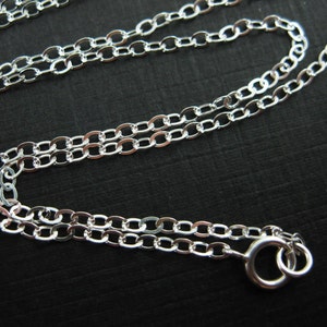 May include: A silver chain necklace with a lobster clasp closure. The chain is made of oval links.