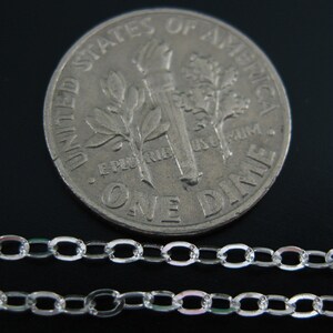 May include: Two silver chains, one on top of the other, are laid out on a black surface. A US dime coin is placed behind the chains for size comparison.