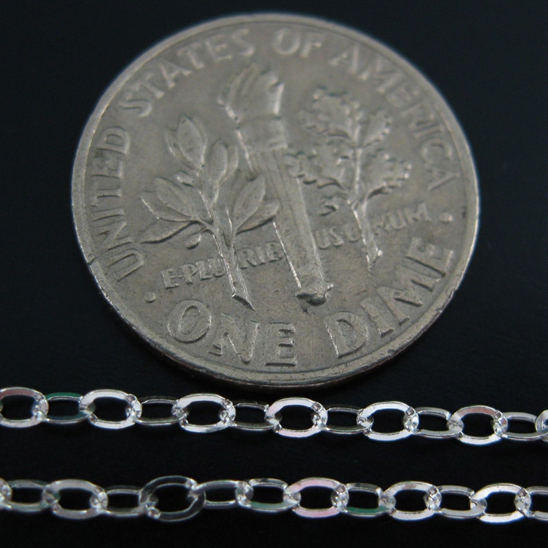 May include: Two silver chains, one on top of the other, are laid out on a black surface. A US dime coin is placed behind the chains for size comparison.
