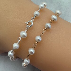 Puede incluir: Una delicada pulsera con perlas blancas ensartadas en alambre de plata y oro. La pulsera tiene un cierre plateado y est&aacute; dise&ntilde;ada para usarse en la mu&ntilde;eca. Las perlas son redondas y est&aacute;n espaciadas uniformemente, creando un aspecto cl&aacute;sico y elegante.