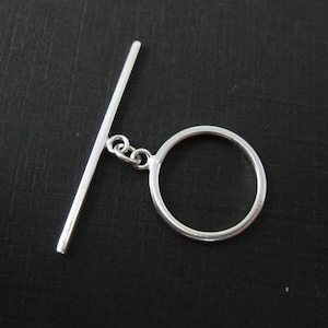 May include: Silver toggle clasp with a round ring and a straight bar. The clasp is made of metal and has a polished finish.