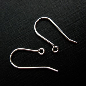 May include: Two silver-colored earring hooks are displayed against a dark background. The hooks have a curved design with a loop at the bottom and a straight wire extending from the top. The hooks are made of a shiny metal.