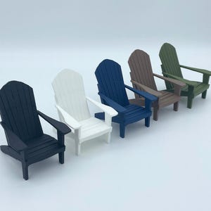 May include: A selection of miniature Adirondack chairs in a row, in colours of black, white, blue, brown, and green. Each chair has a slatted back and armrests, suitable for a doll's house or miniature garden.