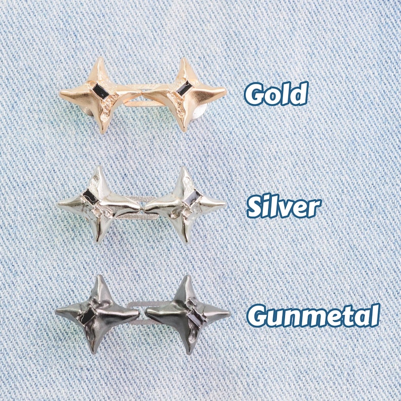 Puede incluir: Tres pares de adornos met&aacute;licos en forma de estrella en acabados dorado, plateado y metal de ca&ntilde;&oacute;n. Cada estrella tiene cuatro puntas y un peque&ntilde;o acento negro. Las palabras "Gold", "Silver" y "Gunmetal" est&aacute;n escritas junto a cada par.
