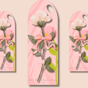 Könnte beinhalten: Drei rosa florale Geschenkanhänger mit einer weißen Blume, grünen Blättern und einer rosa Schleife. Die Anhänger haben eine gebogene Oberseite mit einem Loch und dem Text "Just a little something to make you smile."