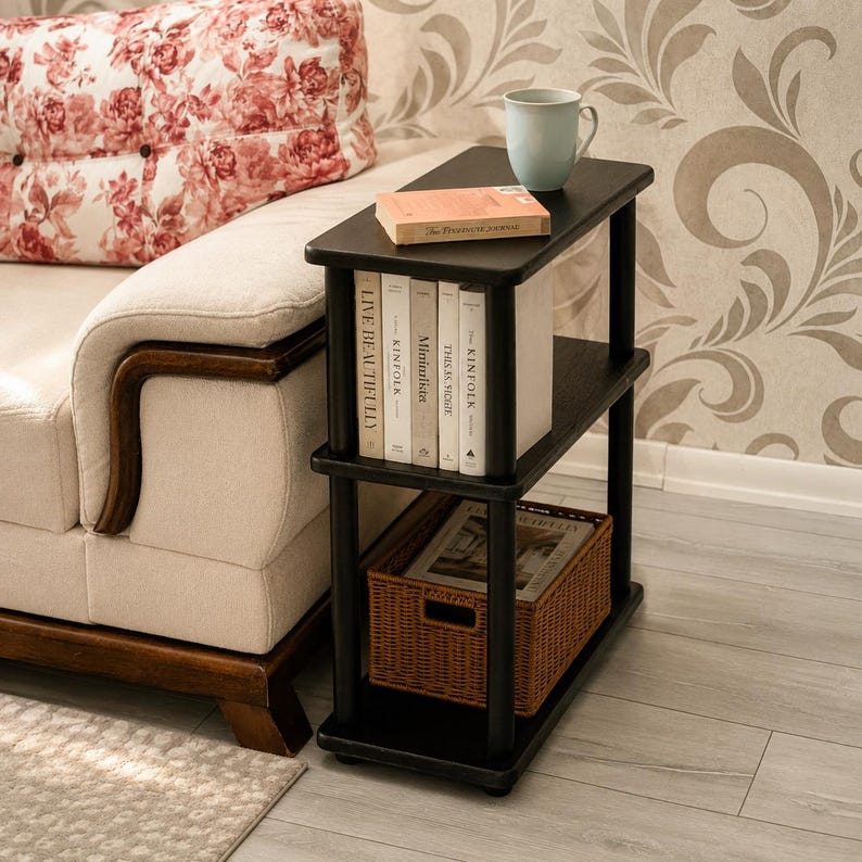 May include: A black three-tier side table with a rectangular top, a middle shelf holding five books titled Live Beautifully, Kinfolk, Minimalista, This Is Sicily, and The Kinfolk, and a bottom shelf containing a woven brown storage basket.
