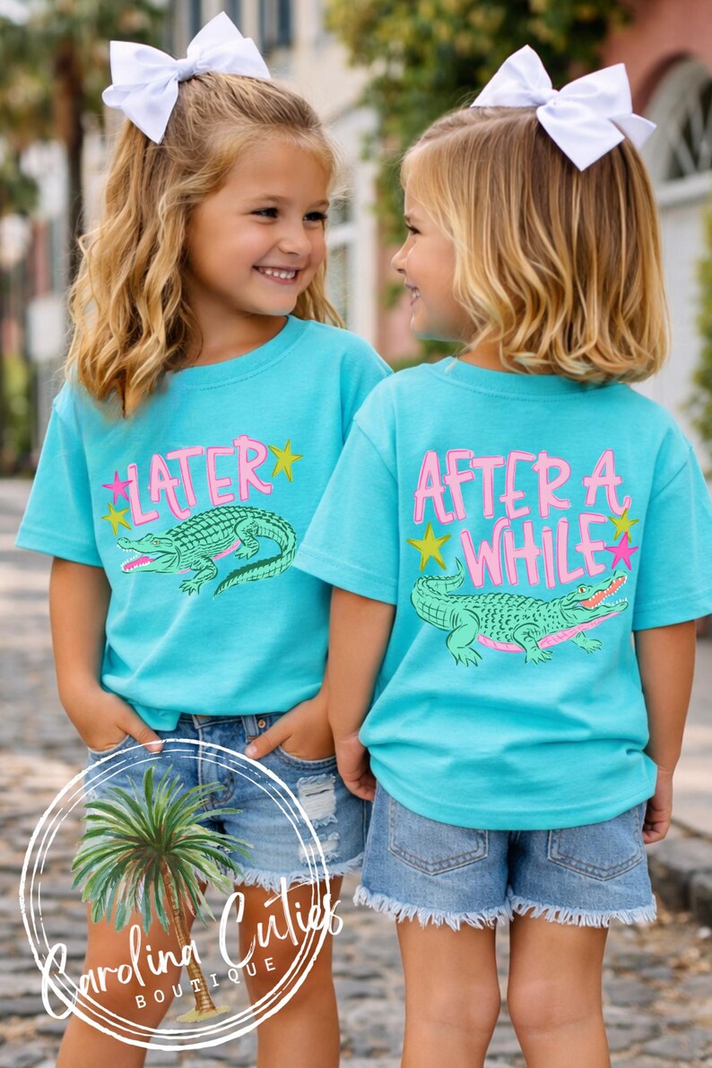 May include: Two young girls wearing matching turquoise t-shirts with alligator graphics and the words "LATER" and "AFTER A WHILE" in pink. They are also wearing denim shorts and white bows in their hair. The shirts are from Carolina Cuties Boutique.