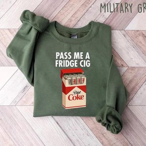 May include: Military green sweatshirt with the text "PASS ME A FRIDGE CIG" and a graphic of a Diet Coke box filled with cans. The sweatshirt is a crew neck style.