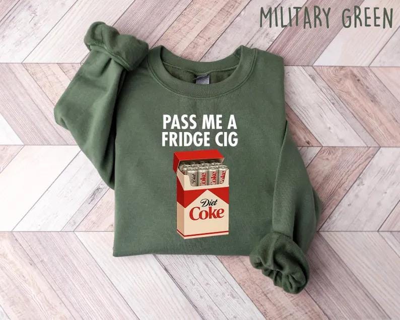 May include: Military green sweatshirt with the text "PASS ME A FRIDGE CIG" and a graphic of a Diet Coke box filled with cans. The sweatshirt is a crew neck style.