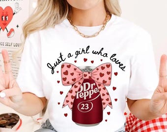May include: White t-shirt with the text "Just a girl who loves" above a Dr Pepper can design. The can is wrapped with a pink bow adorned with red hearts. The number "23" is on the can.